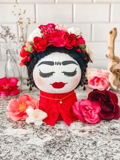 a doll with flowers in her hair sitting on a counter next to some red and white flowers