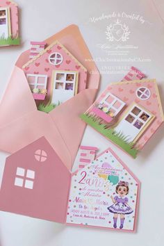 some cards and envelopes are laying on a white surface with pink houses in the background