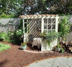 a small garden shed with potted plants and a table in the corner next to it