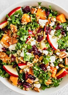 a salad with apples, cranberries, nuts and feta cheese in a white bowl