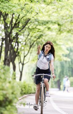 a woman riding a bike down a tree lined street with her hand up in the air