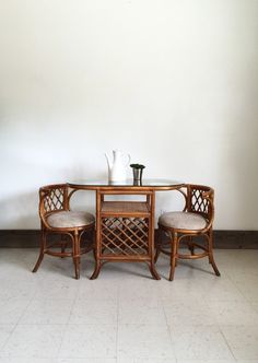 a table with two chairs and a vase on it in front of a white wall