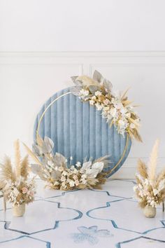 an arrangement of flowers and plants in front of a blue circular mirror on a table