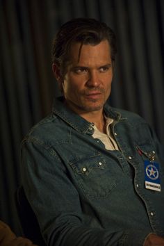 a man wearing a jean jacket with a badge on his left chest and one hand in the other pocket