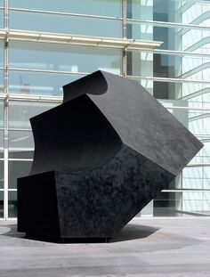 a large black sculpture sitting in front of a tall building