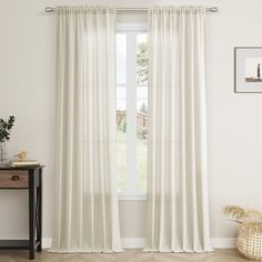 a white curtain hangs in front of a window with a wooden table and vase on the side