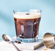 an iced drink with ice and caramel is sitting on a table next to two spoons