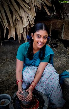 a woman sitting on the ground next to a pot with something in it and smiling at the camera