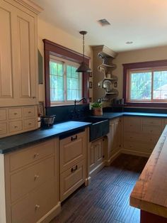 a large kitchen with wooden floors and white cupboards, black counter tops and wood flooring