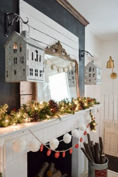 a fireplace mantel decorated for christmas with garland, lights and houses on the mantle