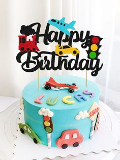 a blue birthday cake with cars and trucks on it, sitting on a white plate