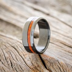 a wedding ring with an orange and black wood inlay sits on a piece of wood