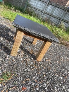 a wooden bench sitting on top of a gravel covered ground next to a yard and fence