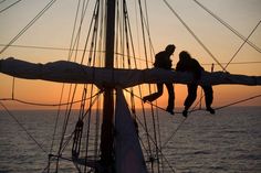 two people climbing up the side of a sailboat at sunset or sunrise on the water