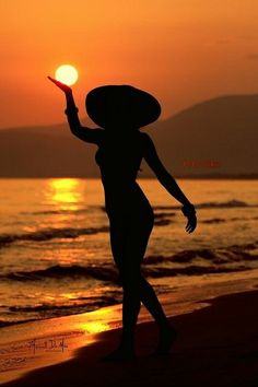 a woman is walking on the beach at sunset with her hand up in the air