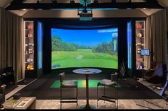 a golf simulator is set up with chairs, tables and televisions on the wall