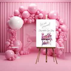 an easel in front of a pink backdrop with balloons and a poster on it