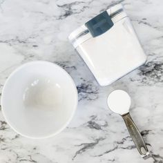 a cup and spoon on a marble counter top next to a container with sugar in it