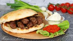 a meatball sandwich with lettuce, tomatoes and sauce on a wooden plate