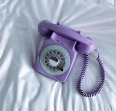 an old fashioned purple phone laying on a white sheet with the cord still attached to it