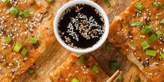 an overhead view of some food on a cutting board with chopsticks and dipping sauce