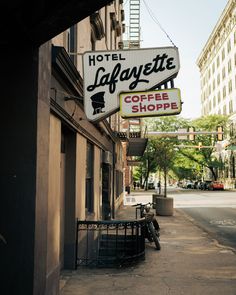 a hotel lafayette coffee shop sign hanging from the side of a building next to a sidewalk