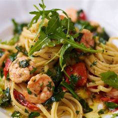 pasta with shrimp, tomatoes and greens on a white plate in a light colored setting