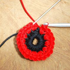 a crocheted red and black flower on a wooden table next to knitting needles