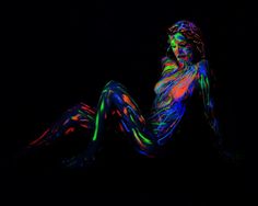 a woman is sitting in the dark with neon paint on her body and legs,