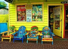 brightly colored chairs line up in front of a yellow building with posters on the wall