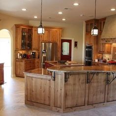 a large kitchen with wooden cabinets and an island in the middle of the room is lit by two pendant lights