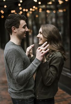 a man and woman standing next to each other in front of a building with lights