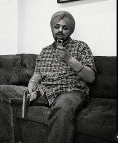 a man in a turban sitting on a couch looking at his cell phone