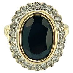 This Art Deco Cocktail Gold Ring is a magnificent statement piece that exudes luxury and sophistication. Crafted in the iconic French style, it embodies the timeless elegance and exquisite craftsmanship synonymous with Art Deco French jewelry design. At the heart of the ring is a breathtaking 6.30-carat sapphire bezel-set, a gemstone prized for its rich color and timeless beauty. The sapphire takes center stage, commanding attention with its intense hue and exceptional clarity. Surrounding the s Luxury Oval Diamond Cut Sapphire Ring, Classic Oval Sapphire Ring, Elegant Yellow Gold Emerald Ring For Formal Events, Elegant Yellow Gold Emerald Ring For Formal Occasions, Classic Oval Sapphire Ring With Diamond Accents, Elegant Evening Rings With Center Stone, Classic Diamond White Gemstone Rings, Exquisite Oval Diamond Ring For Formal Occasions, Elegant Evening Diamond Ring With Gemstone