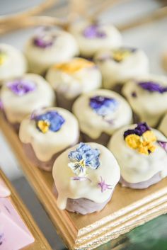 there are many small desserts on the tray with purple and yellow flowers in them