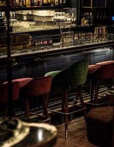 a bar with several stools and bottles on the back wall, in front of it is a row of empty wine glasses