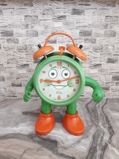 an orange and green alarm clock sitting on top of a stone floor next to a brick wall