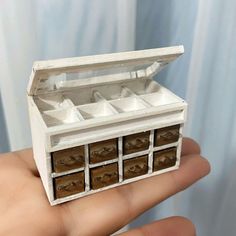 a hand holding a miniature white box with drawers on it's sides and the lid open