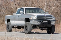 a silver truck parked on the side of a dirt road in front of some trees