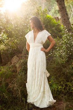 a woman wearing a white dress standing in the woods with her hands on her hips