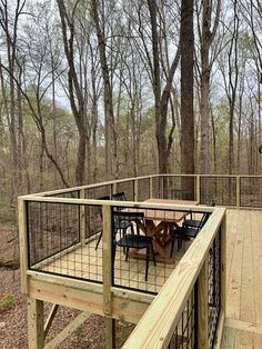 a wooden deck with metal railings and table on it in front of some trees