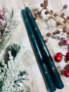 two blue candles sitting on top of a table next to berries and pine cones with gold stars