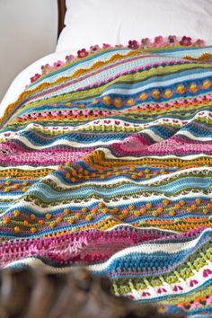 a crocheted blanket sitting on top of a bed next to a wooden headboard