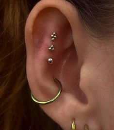 a woman wearing gold ear piercings with four small balls on the side of her ear