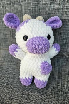 a crocheted purple and white stuffed animal sitting on a gray fabric chair with black eyes