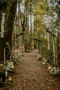 a path in the middle of a forest with white flowers and candles on each side