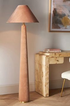 a lamp that is next to a desk with a chair in front of it and a painting on the wall