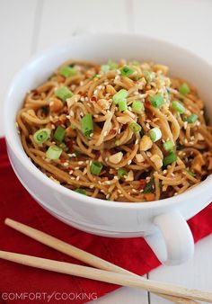 a white bowl filled with noodles and veggies next to chopsticks on a red napkin