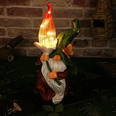 an illuminated gnome figurine sitting on top of a brick wall next to a lit candle