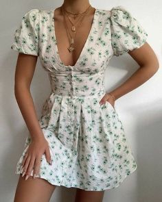 a woman wearing a white dress with green flowers on it, posing for the camera